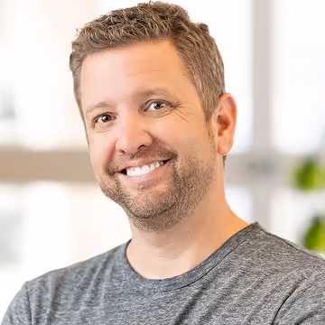 Chris Riley headshot smiling into the camera in the grey t-shirt